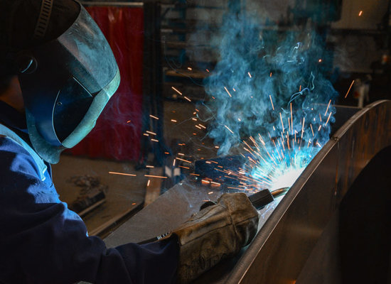 Schweißer mit Helm bei der Bearbeitung eines Metallbauteils mit sichtbaren Lichtbögen
